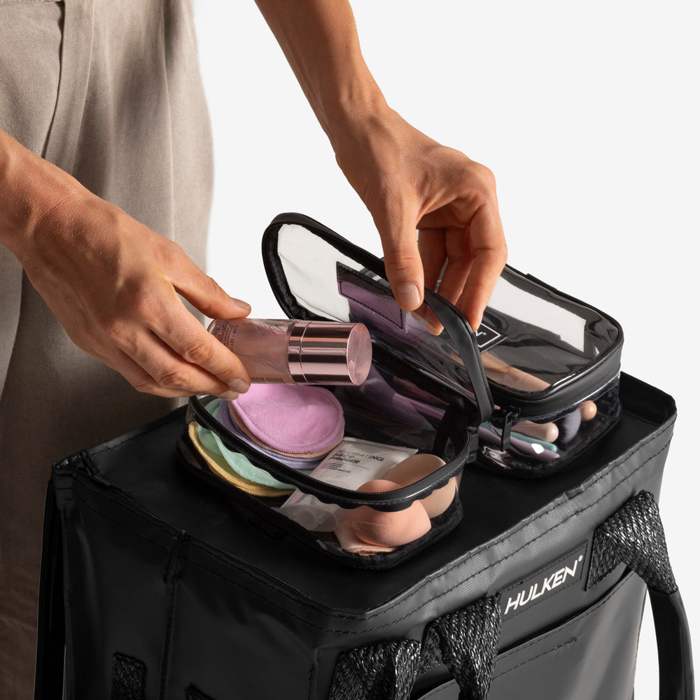 Person opening a black makeup bag with cosmetic items