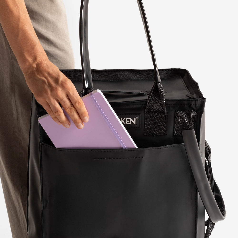 Person placing a purple notebook into a black bag 