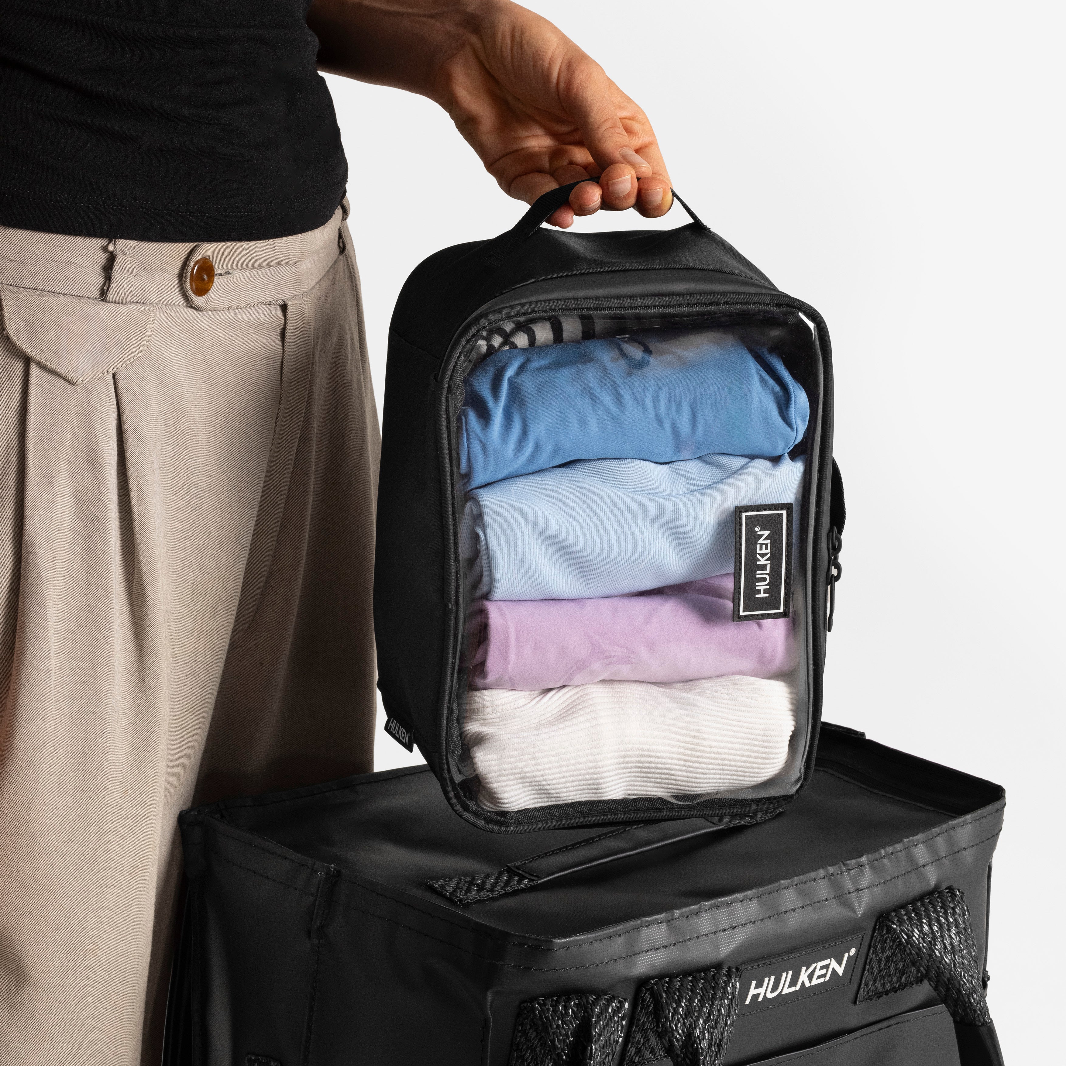 Person holding a black Hulken packing case with clothes inside