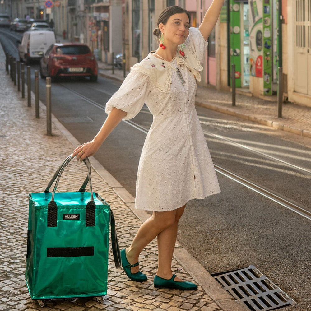 Woman in a white dress walking with a teal tote bag on a city street